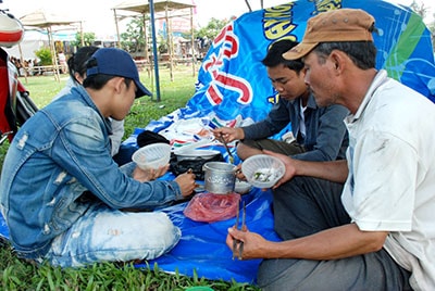 Tranh thủ trải tấm bạt, ông Trần Quốc Hùng và các cháu ăn vội bữa cơm trưa đạm bạc để lấy sức bán hoa.