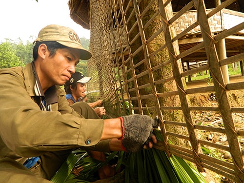 Người dân thôn R’bhướp giúp nhau kết lá cọ lợp mái nhà nơi ở mới.  Ảnh: BHƠRIU QUÂN