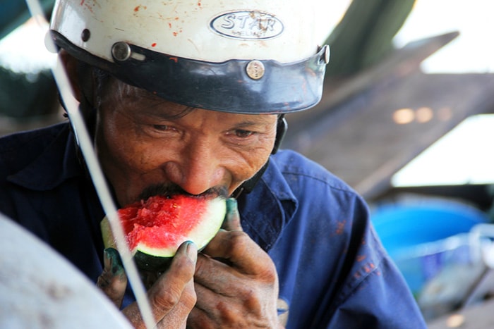 Ông Hiệu, một thợ sửa tàu ăn vội dưa hấu rồi tiếp tục công việc để kịp “tiến độ”.