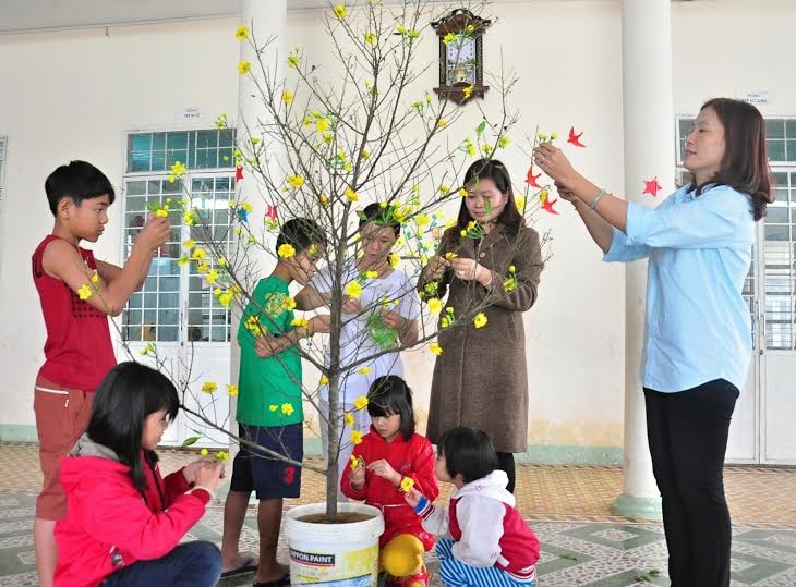 Các “mẹ” và trẻ em Trung tâm Trẻ mồ côi sơ sinh Quảng Nam trang trí cành mai đón tết. Ảnh: VINH ANH. 