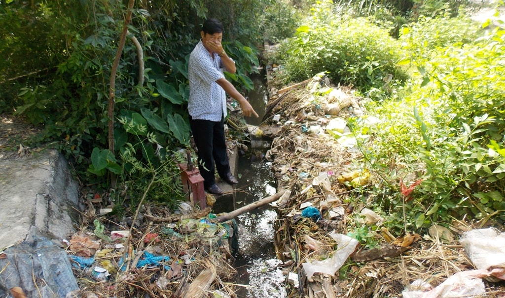 Ông Cảnh chỉ đoạn kênh mương bị ùn ứ rác thải, xác gia cầm bốc mùi hôi thối. Ảnh: XUÂN KHÁNH