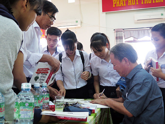 Nhà văn, nhạc sĩ Vũ Đức Sao Biển ký tặng sách cho học sinh Duy Xuyên.  Ảnh: SONG ANH