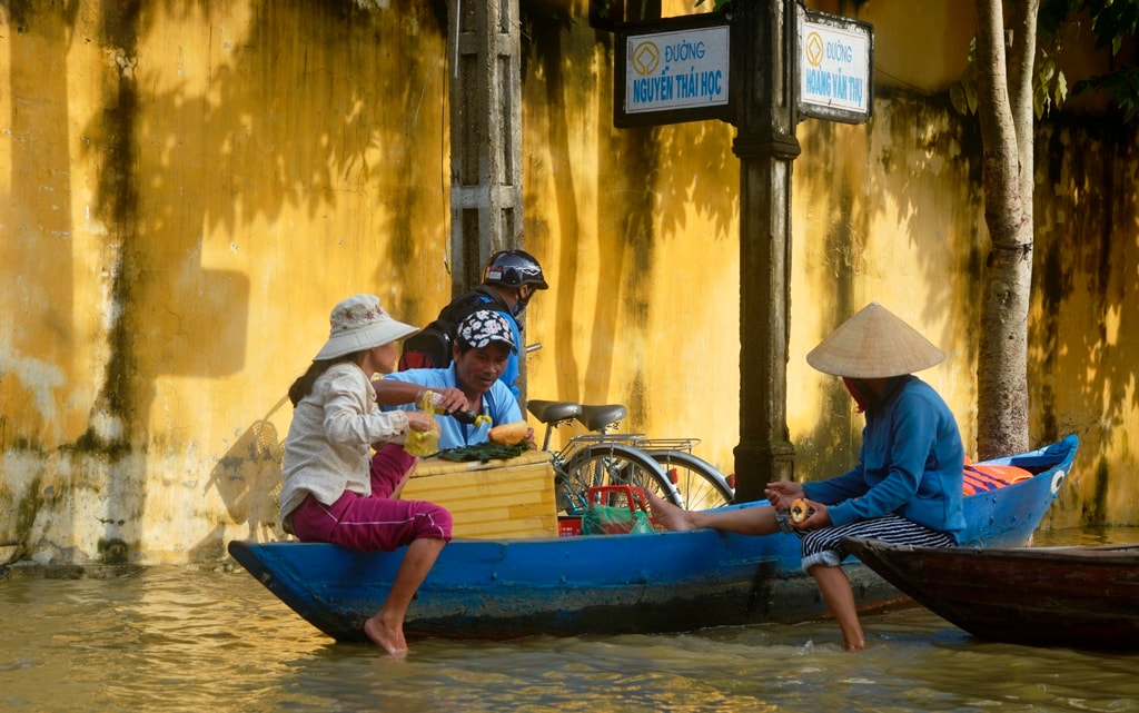 Người đàn ông bán bánh mì dạo đang làm bánh mì cho khách của mình là những người chèo thuyền chở khách du lịch. Bỏ bánh mì vào thùng xốp, đó là cách để người đàn ông này hạn chế thấp nhất rủi ro khi lội nước bán bánh mì, bên cạnh giữ độ giòn, nóng của bánh mì. Ảnh: XUÂN THỌ