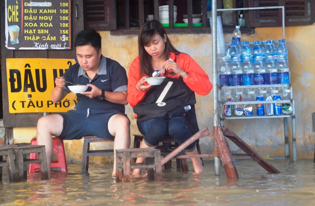 Đôi bạn trẻ này vẫn quyết tâm thưởng thức các món ăn vỉa hè ở Hội An, dù dưới chân họ là nước lũ. Ảnh: XUÂN THỌ