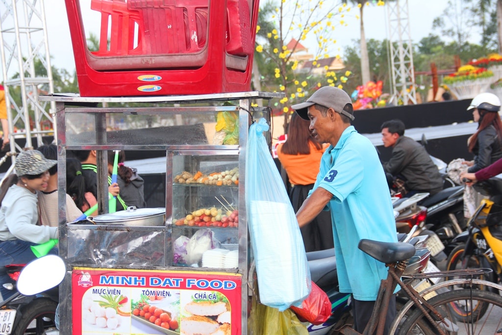 Dù bên cạnh dòng người tìm vui xuân đông đúc nhưng người đàn ông này vẫn miệt mài đẩy chiếc xe chở các món hàng xiên que, mực viên, chả cá,... bán cho khách đi đường. Ảnh: A.N