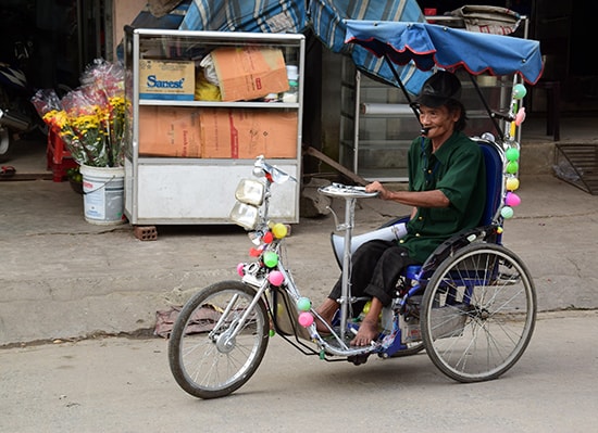 Bất kể nắng mưa, ông Hai vẫn lăn bánh xe đi quanh chợ Trung Phước tuyên truyền giữ gìn an ninh trật tự.  Ảnh: DƯƠNG THẮNG