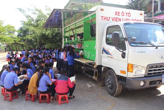 Các em học sinh chăm chú đọc sách từ xe thư viện lưu động.