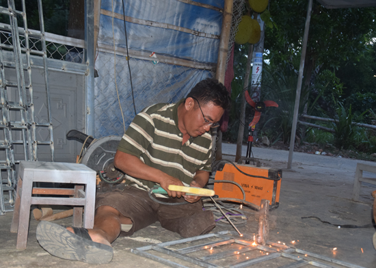 Anh Tùng đang cố gắng làm cơ khí trên đôi chân tật nguyền.  Ảnh: DƯƠNG THẮNG