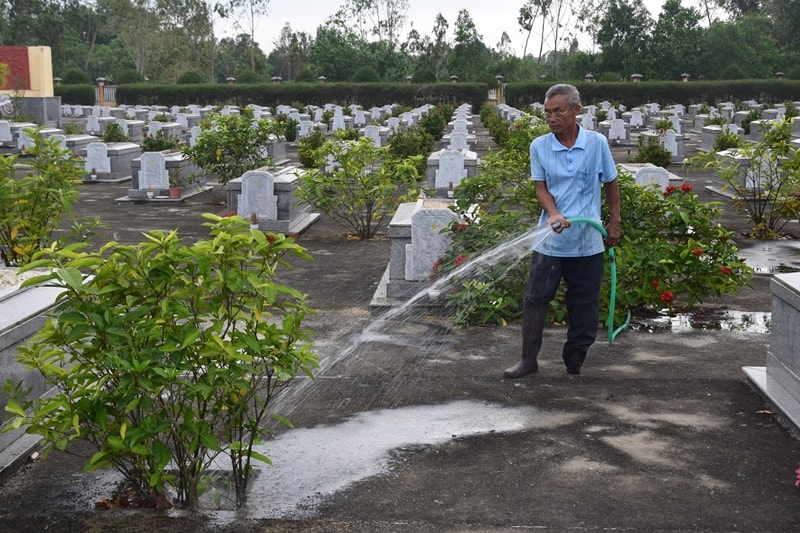 Ông Nguyễn Sư ngày ngày tưới nưới cho cây ở Nghĩa trang liệt sĩ xã Tam Thăng. Ảnh: THANH THẮNG