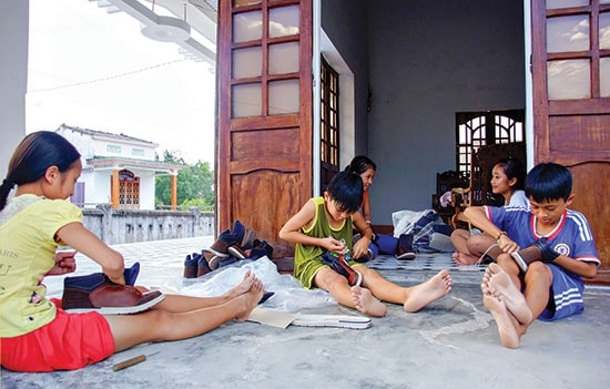 Tranh thủ ngày nghỉ cuối tuần, các em nhỏ ở làng biển Bình Minh - Thăng Bình nhận giày về may gia công.Ảnh: PHƯƠNG THẢO