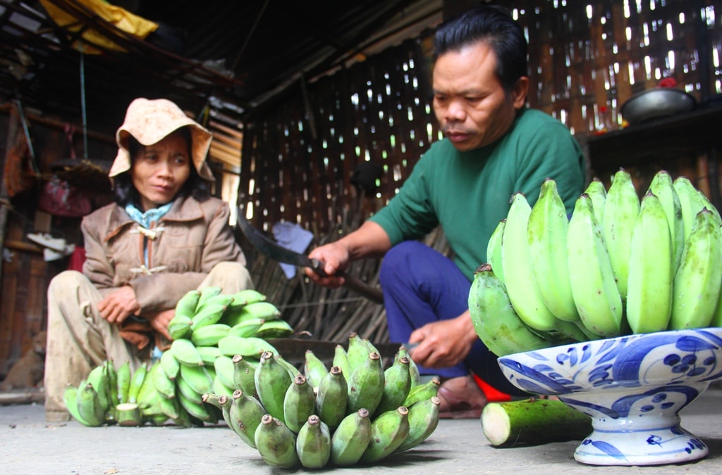 Bên góc bếp, một cặp vợ chồng cùng cắt từng nải chuối mốc trang trí gian thờ tổ tiên.