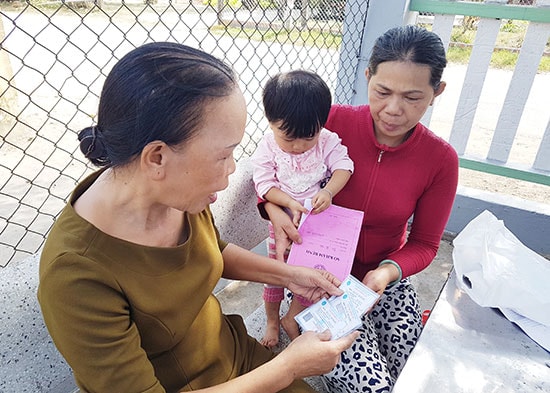 Bà Võ Thị Thuận (bên trái) - đại lý thu của xã Tam Giang đến tận nhà người dân giao thẻ BHYT và nói rõ những quy định mới ghi trên thẻ BHYT cho người dân hiểu. Ảnh: D.L