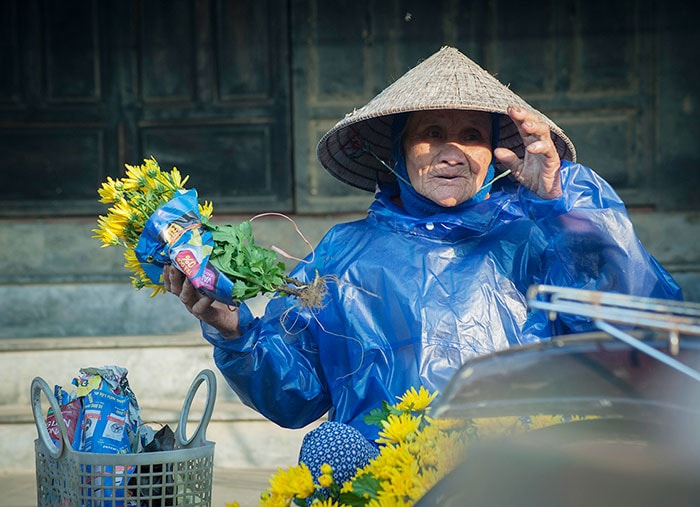 Cụ bà một tay trao hoa một tay che nắng. 