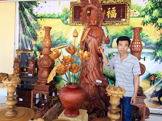Anh Phan Phước Tuấn bên những sản phẩm do cơ sở Gỗ mỹ nghệ Gò Nổi chế tác. Ảnh: VĂN MẾN