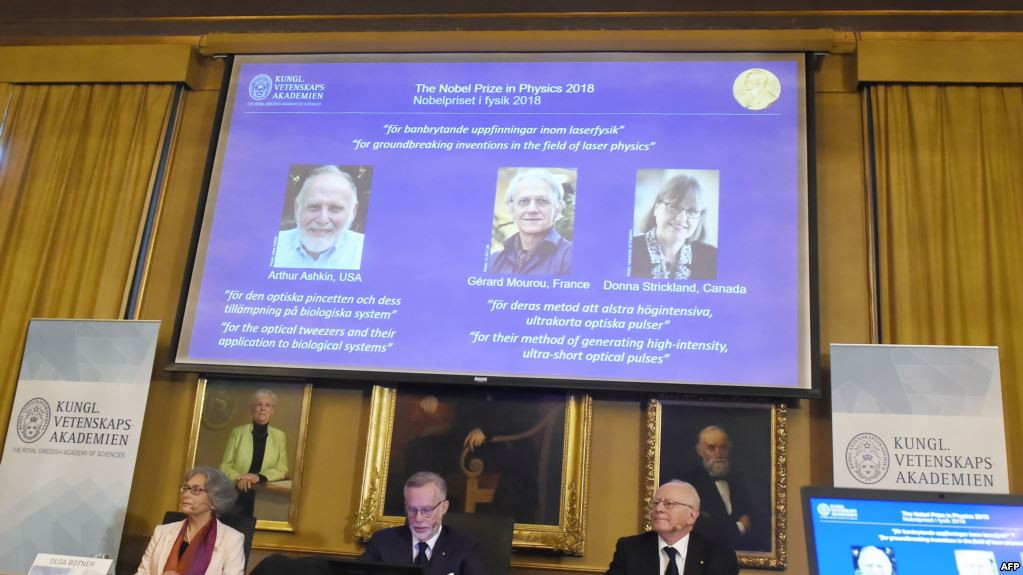 Các thành viên của Ủy ban Nobel Vật lý ngồi trước màn hình trưng bày chân dung các khoa học gia Arthur Ashkin người Mỹ, Gerard Mourou người Pháp và Donna Strickland người Canada trong công bố giải Nobel Vật lý năm 2018. Ảnh: AFP