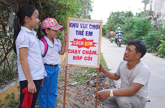 Ông Đặng Hữu Điền (bên phải) tự nguyện đóng cọc và treo bảng lưu ý người điều khiển xe trên đoạn đường có nhiều trẻ em vui chơi. Ảnh: NHƯ TRANG