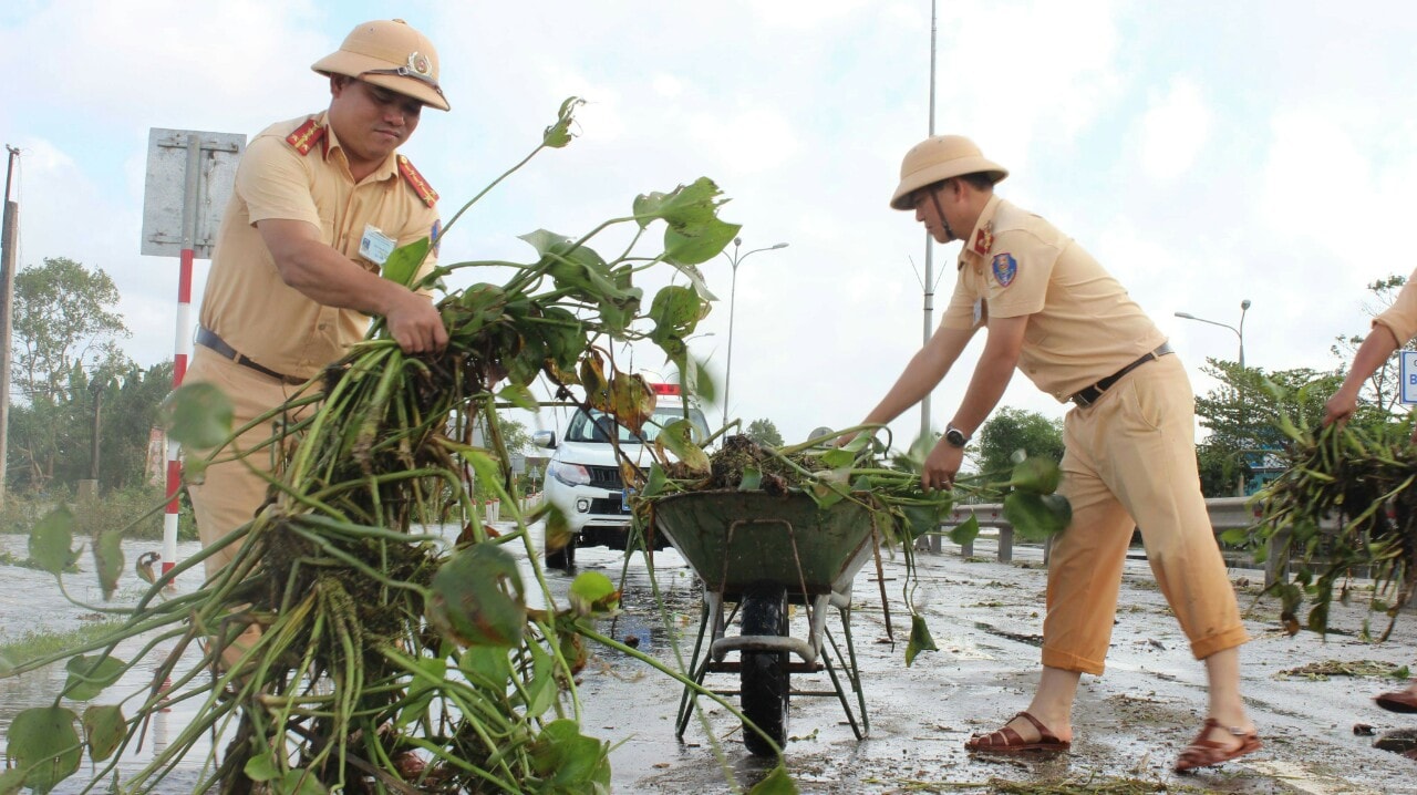 ...và dọn dẹp bèo rác bị nước lũ cuốn tràn lên quốc lộ để xe cộ lưu thông. Ảnh: T.H