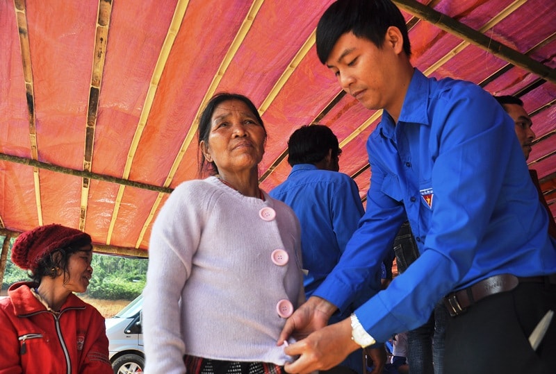 Thanh niên tình nguyện giúp một phụ nữ mặc chiếc áo mới do đoàn trao tặng. Ngoai gạo, nhu yếu phẩm, trong chương trình đoàn còn trao tặng nhiều áo ấm, giày dép cho người dân. Ảnh: VINH ANH