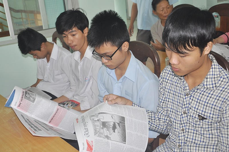 Trong khi chờ buổi lễ bắt đầu, các em học sinh nhận giải tranh thủ đọc Báo Quảng Nam. Ảnh: X.P