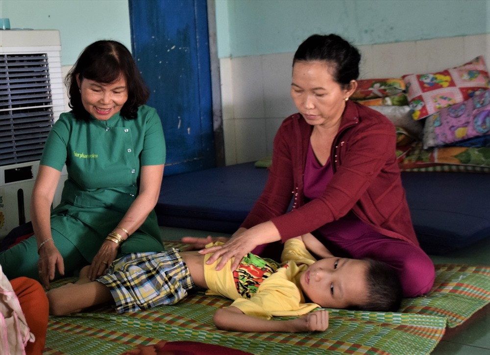 Cô Lê Thị Lý áo xanh đang tập vật lý trị liệu cho trẻ khuyết tật ở Trung tâm Phục hồi chức năng trẻ khuyết tật huyện Phú Ninh. Ảnh: THANH THẮNG