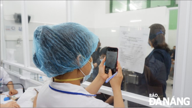 Nhân viên y tế Bệnh viện Đà Nẵng tiếp nhận thông tin bệnh nhân nghi nhiễm SARS-CoV-2 để khám, thông qua lớp kính cách ly. Ảnh: PHAN CHUNG