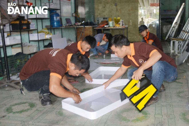 Anh Nguyễn Nhựt (phải) hướng dẫn thợ thi công bảng hiệu đèn led. Ảnh: LÊ VĂN THƠM
