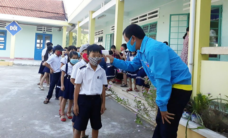 Đoàn viên xã Bình Trung (Thăng Bình) hỗ trợ đo thân nhiệt cho học sinh trước khi vào lớp. Ảnh: K.L
