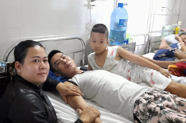 Anh Phạm Thanh Phong (ở giữa) bên vợ con trong những ngày điều trị ở bệnh viện. Hiện Phong nằm liệt một chỗ ở nhà. Ảnh: B.H