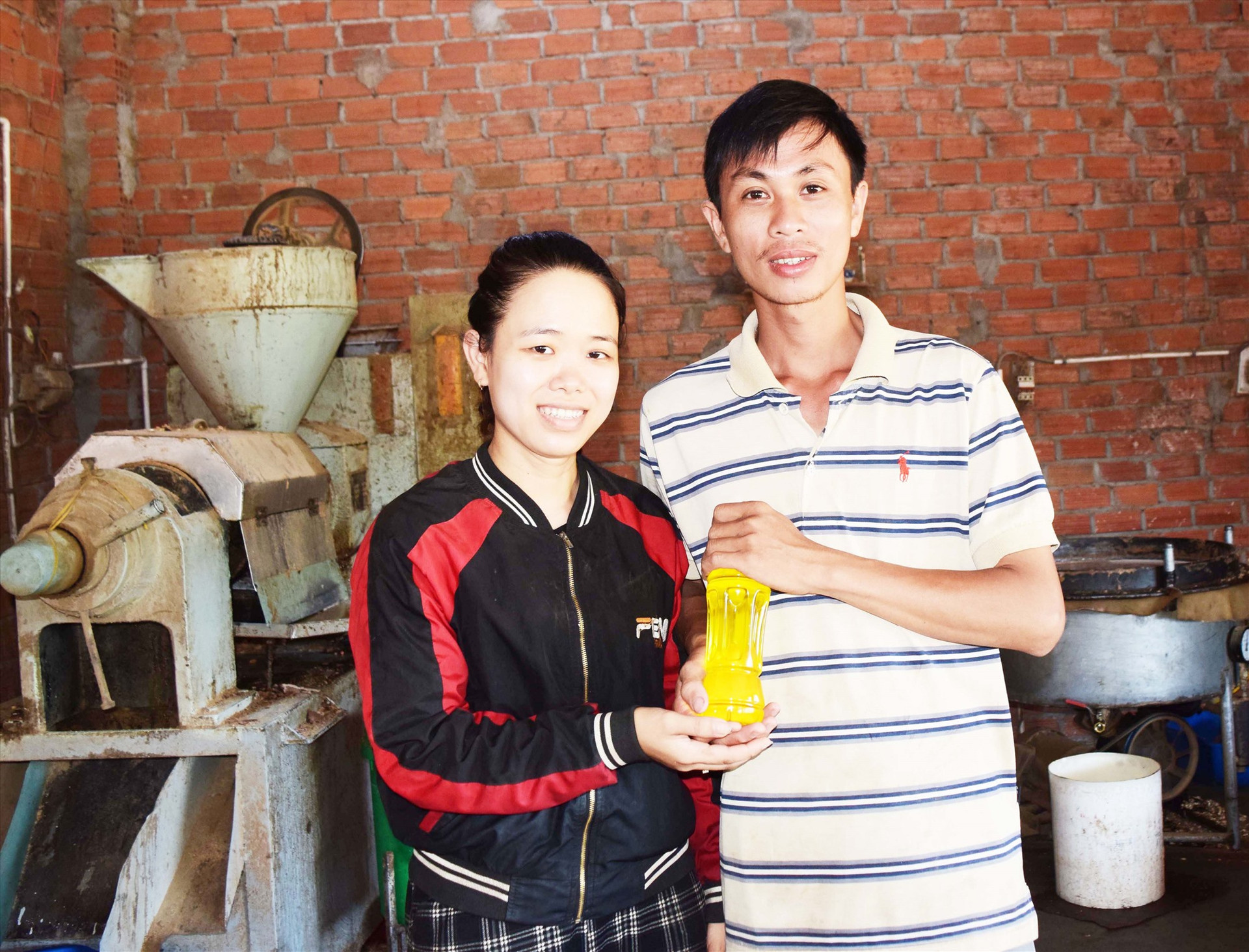 Vợ chồng anh Nguyễn Văn Lâm với sản phẩm dầu được cho ra từ chiếc máy ép công nghiệp đầu tiên của xã. Ảnh: THÁI CƯỜNG