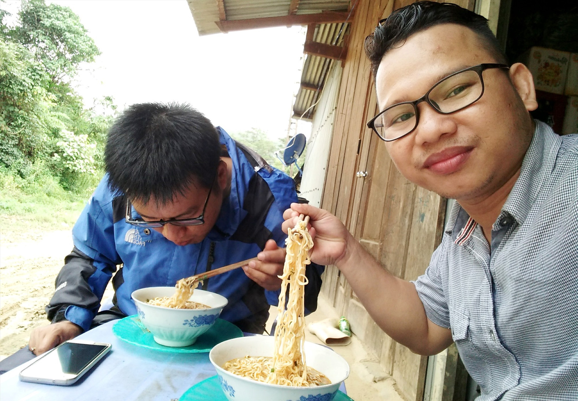 Tác giả (bên phải) cùng đồng nghiệp ăn vội tô mì tôm trên đường tác nghiệp lên biên giới Tây Giang. Ảnh: A.N