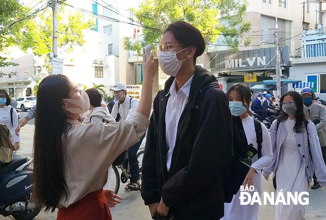 Tại các trường THPT, nhà trường bố trí Đoàn Thanh niên, giáo viên, nhân viên y tế đo thân nhiệt học sinh trước cổng trường. Các em học sinh cũng như giáo viên bảo đảm khoảng cách an toàn khi vào lớp. Trong ảnh: Giáo viên Trường THPT Trần Phú đo thân nhiệt cho học sinh.