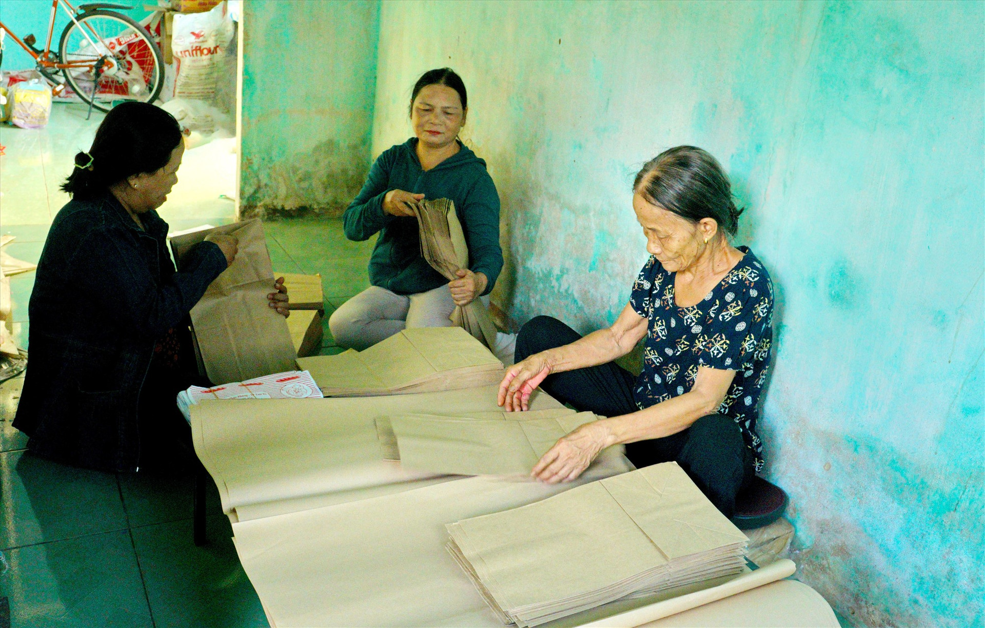 Chị em Chi hội phụ nữ hỗ trợ bà Nguyễn Thị Lê (bìa phải) làm túi giấy. Ảnh: NGUYỄN ĐIỆN NGỌC
