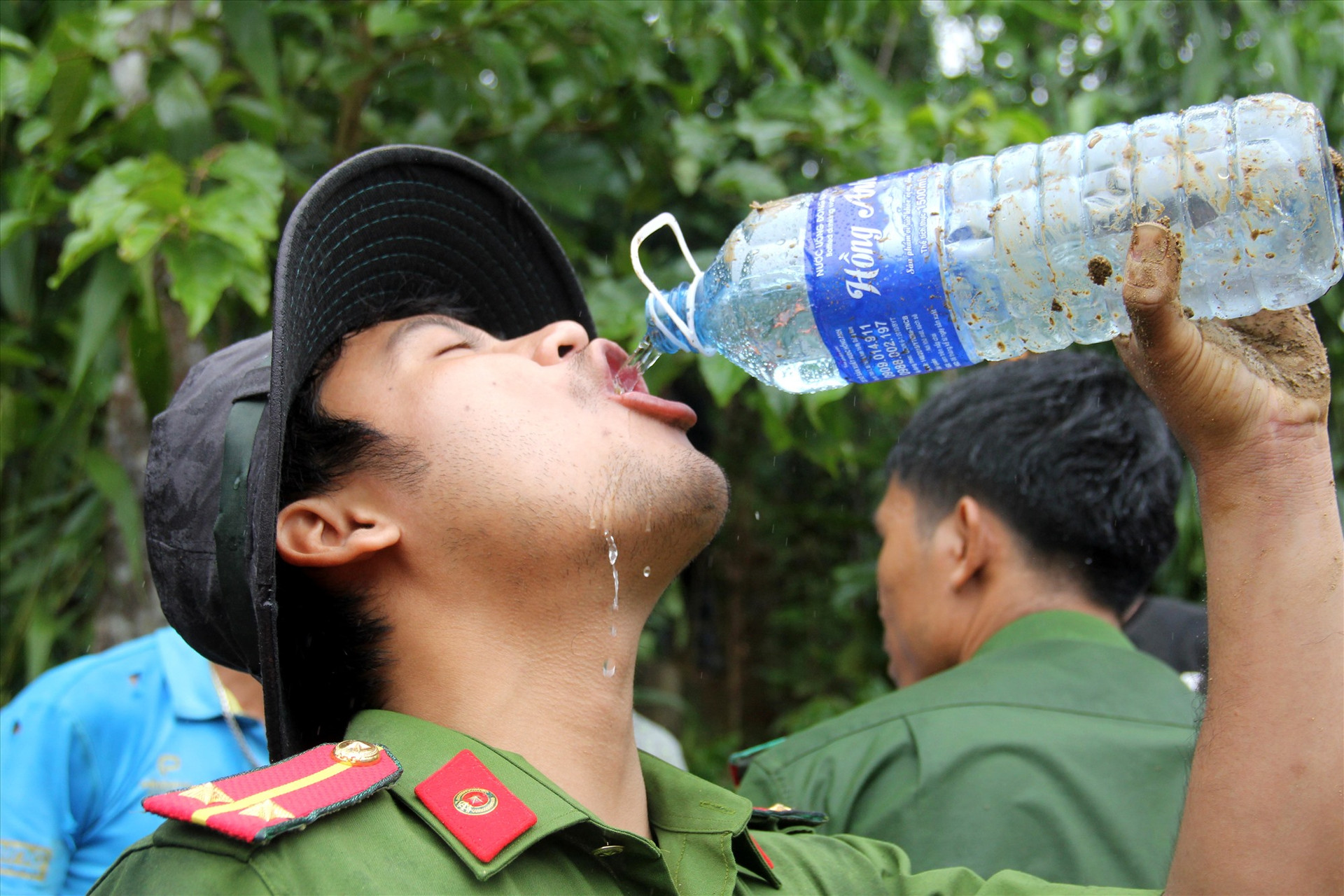 Một chiến sĩ công an uống vội nước. Trên tay lấm lem bùn đất. Ảnh: P.V