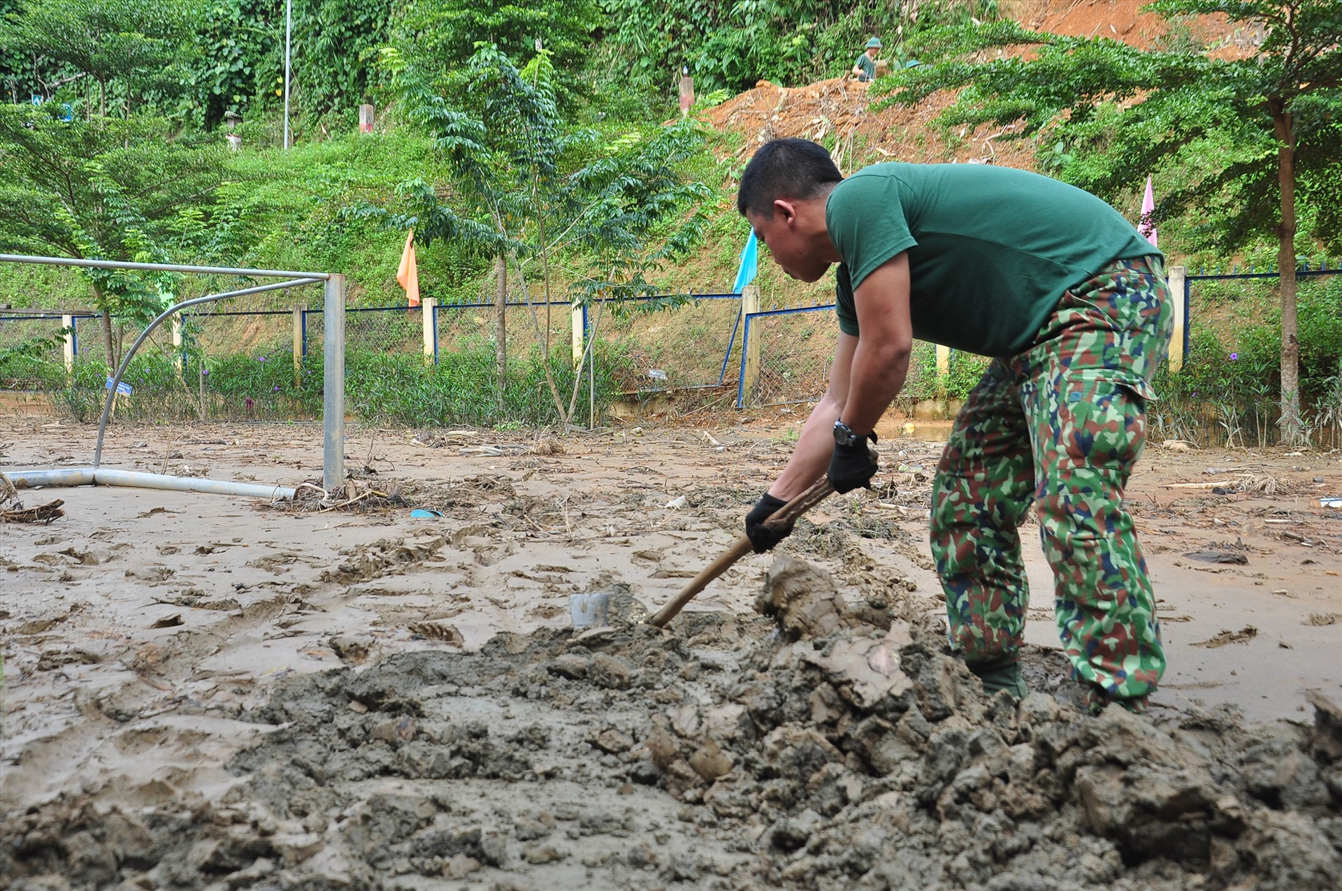Một chiến sĩ đang cố gắng cào lớp bùn đất dày đặc, dính chặt trên sân trường. Ảnh: VINH ANH
