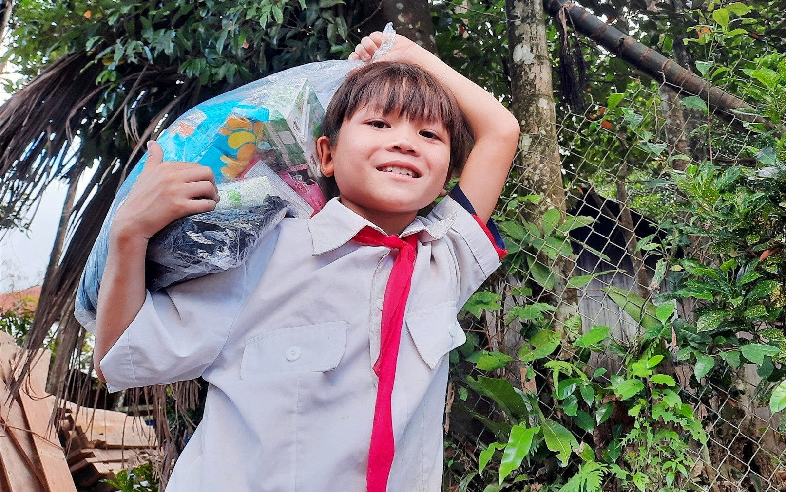 Một cậu học sinh làng Tăk Pát vui mừng vì được áo quần, bánh kẹo do địa phương hỗ trợ. Ảnh: HỒ QUÂN