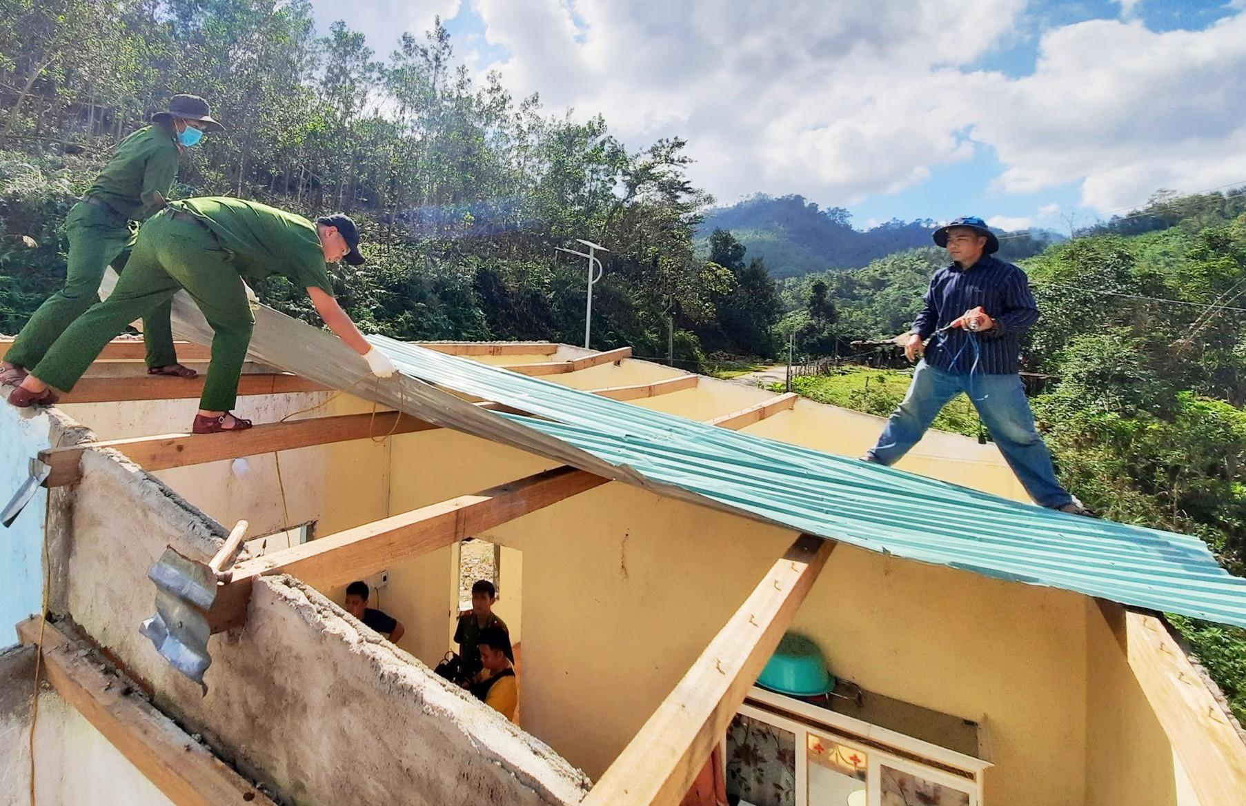 Ra quân tháo dỡ phần mái nhà cũ của một người dân ở Bắc Trà My bị bão thổi bay và lợp lại mái mới. Ảnh: HỒ QUÂN