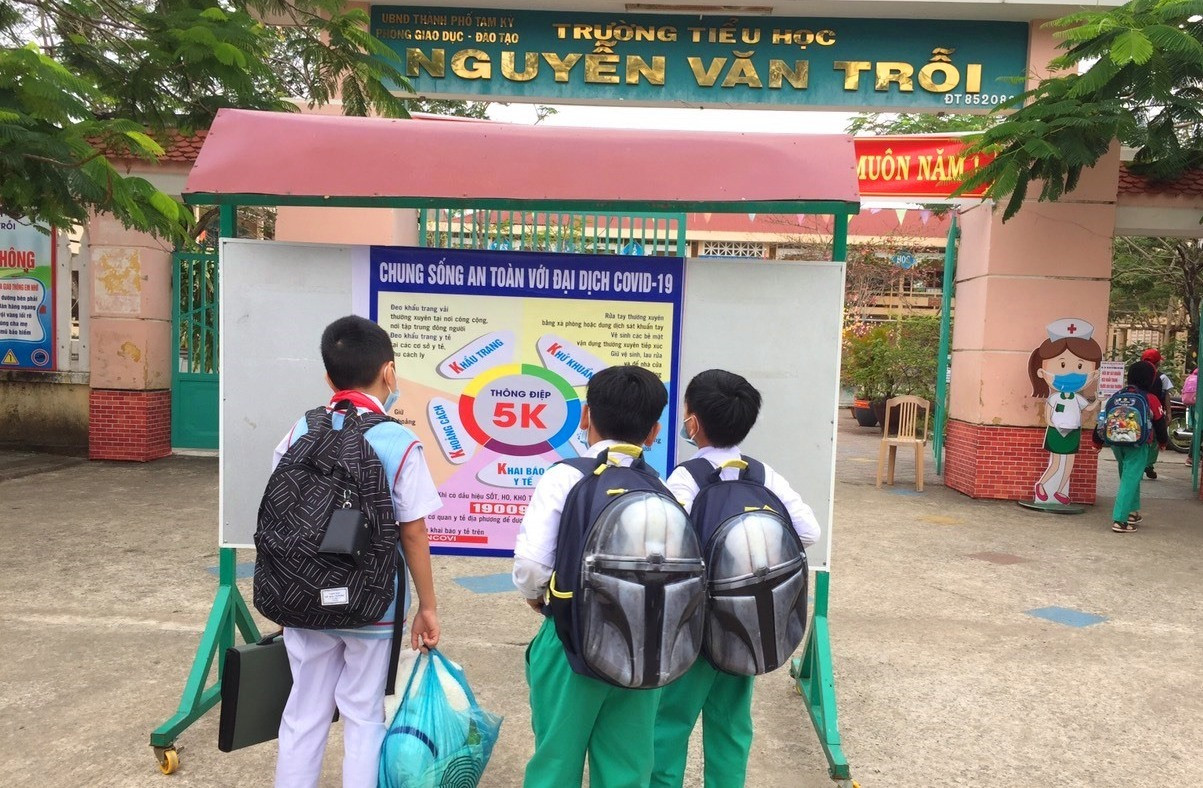 Học sinh Trường Tiểu học Nguyễn Văn Trỗi (Tam Kỳ) xem khuyến cáo phòng chống dịch Covid-19 đặt trước cổng trường. Ảnh: C.N