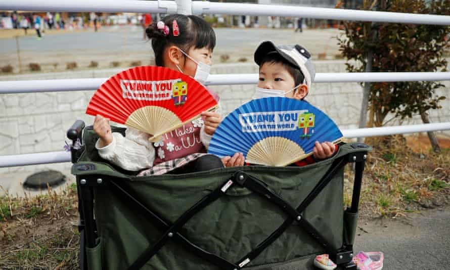 Những đứa trẻ đeo khẩu trang ôm người hâm mộ khi họ chờ đợi dọc theo tuyến đường của lễ rước đuốc Olympic Tokyo 2020, trong trận đại dịch coronavirus Ảnh: Issei Kato / Reuters