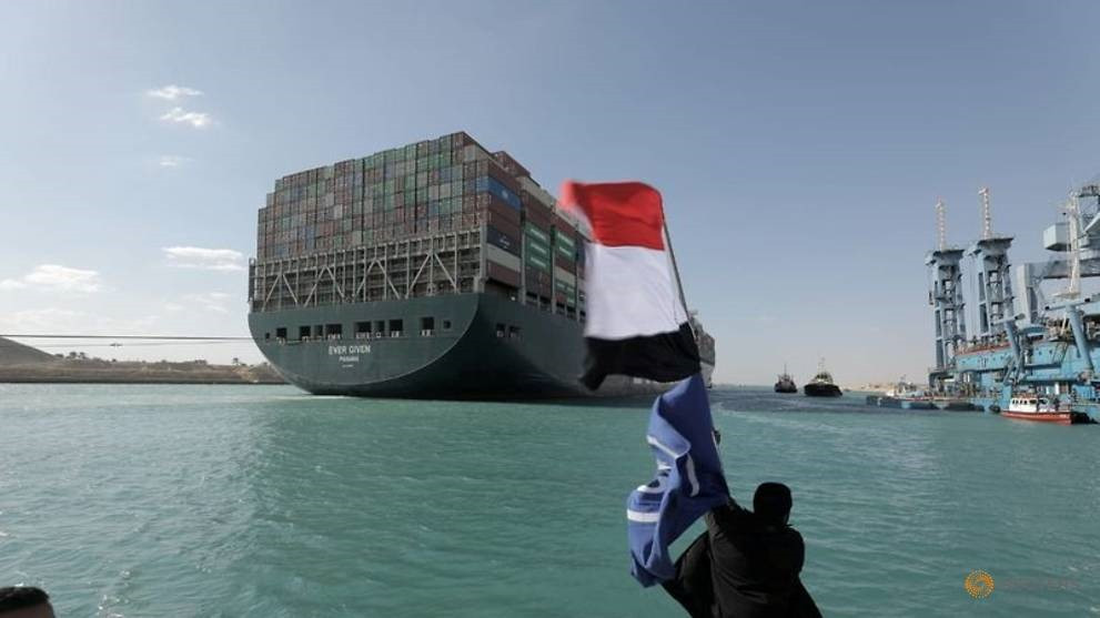 Một người đàn ông vẫy cờ Ai Cập khi tàu Ever Given, một trong những tàu container lớn nhất thế giới, được nhìn thấy sau khi nó được thả trôi hoàn toàn ở kênh đào Suez, Ai Cập vào ngày 29 tháng 3 năm 2021. Cơ quan quản lý kênh đào Suez / Handout via REUTERS