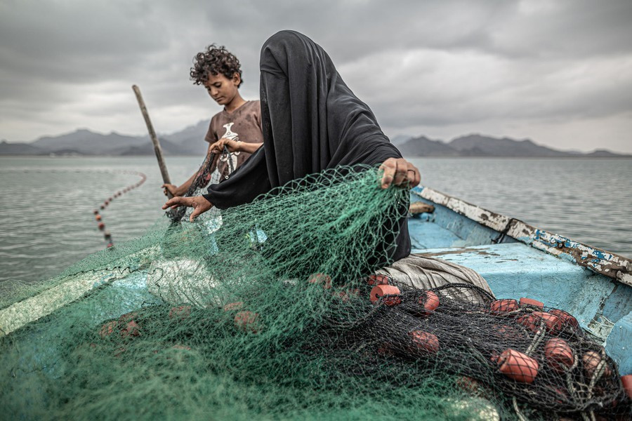 Fatima và con trai chuẩn bị lưới đánh cá trên một chiếc thuyền ở vịnh Khor Omeira, Yemen, vào ngày 12 tháng 2. Fatima có chín người con. Để cung cấp cho họ, cô ấy kiếm sống bằng nghề đánh cá. Mặc dù ngôi làng của cô bị tàn phá bởi xung đột vũ trang ở Yemen, Fatima vẫn quay lại tiếp tục sinh kế, mua một chiếc thuyền bằng số tiền kiếm được từ việc bán cá. Xung đột - giữa phiến quân Hồi giáo dòng Shia Houthi và liên minh Ả Rập dòng Sunni do Ả Rập Xê-út dẫn đầu - bắt đầu từ năm 2014 và đã dẫn đến điều mà UNICEF gọi là cuộc khủng hoảng nhân đạo lớn nhất thế giới. Khoảng 20,1 triệu người (gần 2/3 dân số) yêu cầu hỗ trợ lương thực vào đầu năm 2020, với khoảng 80% dân số dựa vào viện trợ nhân đạo. #