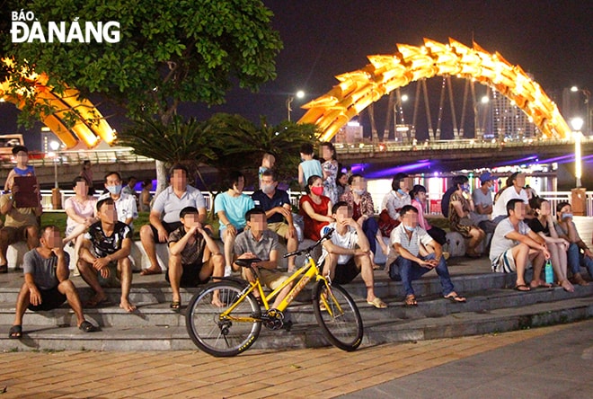 Nhiều người dân tập trung thành nhóm đông người xem chương trình nghệ thuật gần khu vực cầu Rồng nhưng không đeo khẩu trang. (Ảnh chụp tối 27-4).