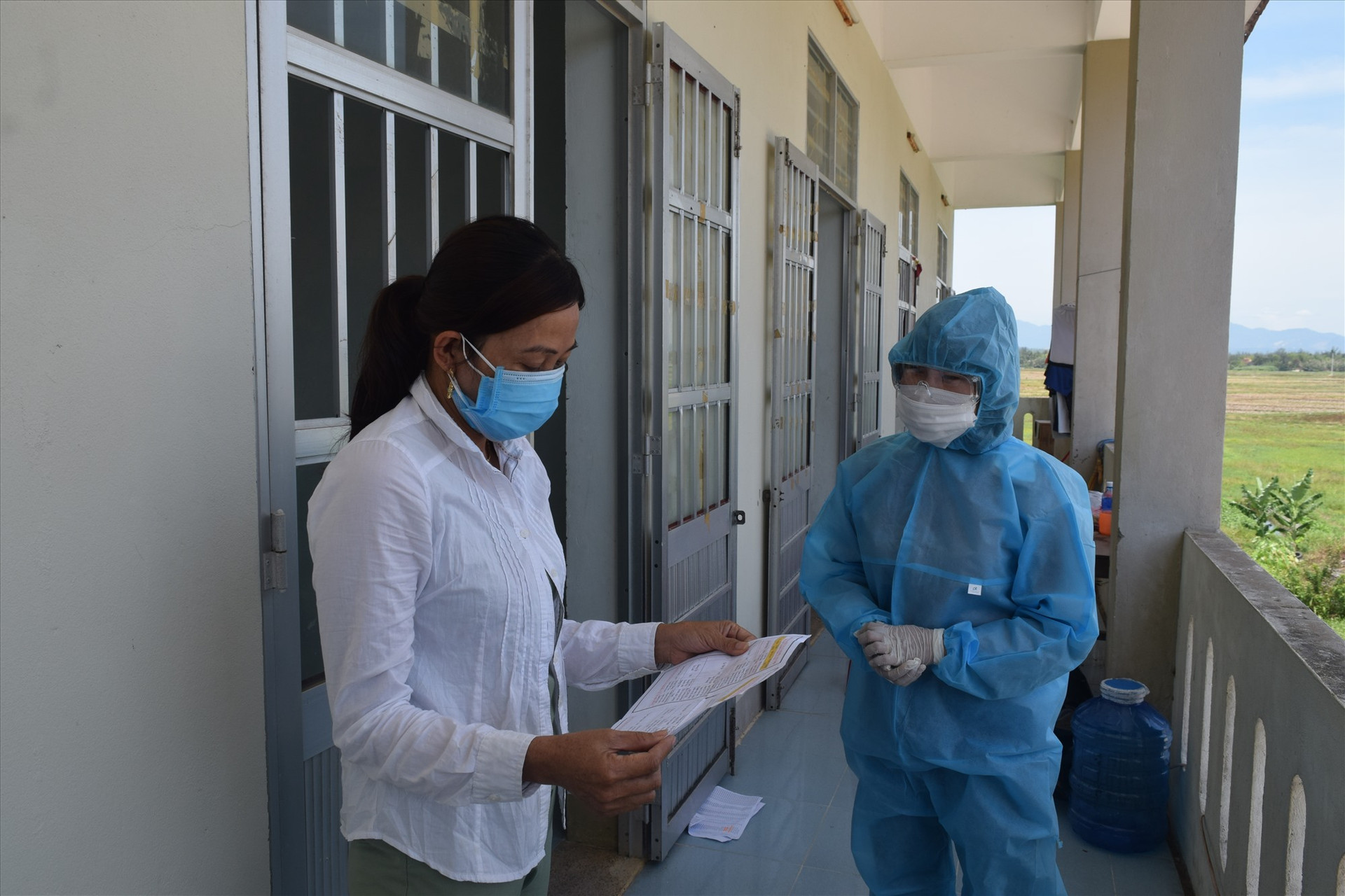 Công dân khu cách ly tập trung tại Nhà đa năng và Trạm y tế xã Bình Đào đang xem danh sách ứng cử viên được in trên tờ rơi