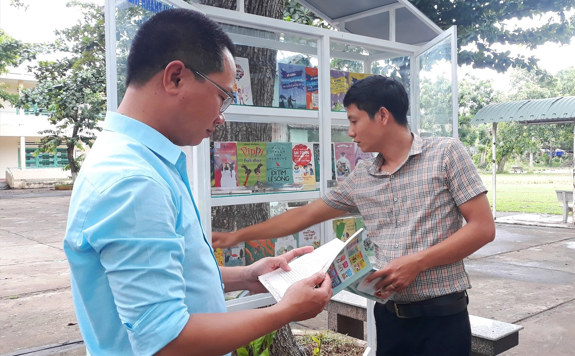 Thầy Tăng Văn Chung (trái) và thầy Nguyễn Khắc Việt đọc sách ở “cây sách” sân trường. Ảnh: C.N