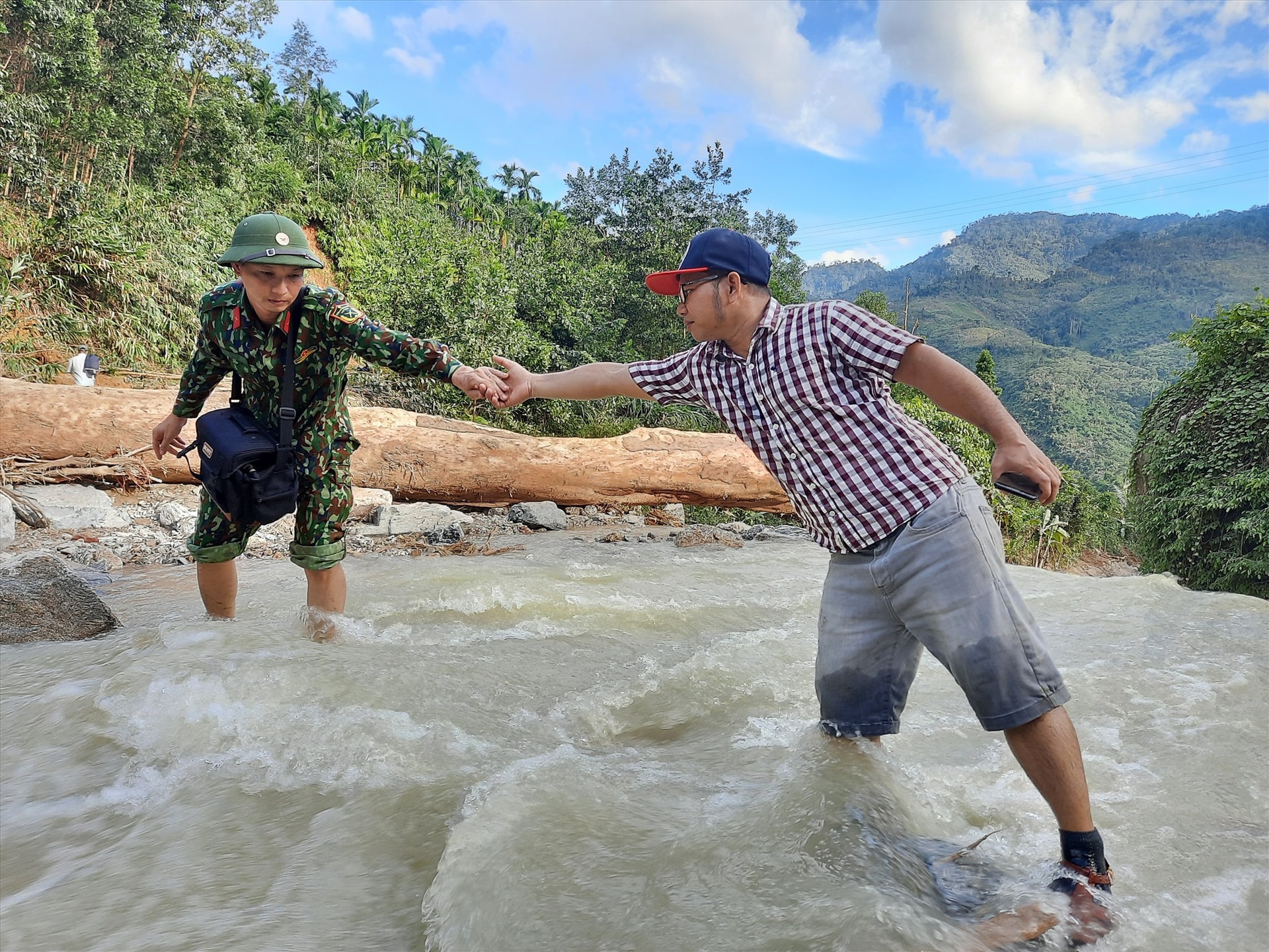 Nhà báo Alăng Ngước (bên phải) hỗ trợ đồng nghiệp kênh Truyền hình Quốc phòng Việt Nam vượt lũ trên chuyến tác nghiệp tại Trà Leng. Ảnh: Đ.N