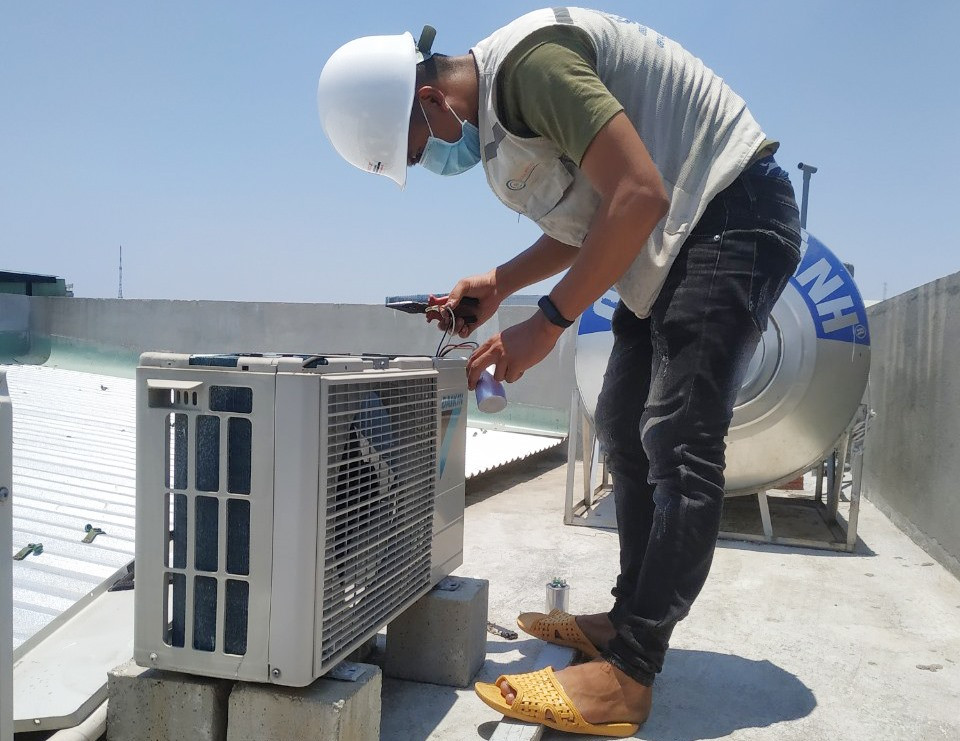 Người thợ điện lạnh lắp dây đồng vào cục nóng điều hòa trên sân thượng tầng 4 với nhiệt độ ngoài trời chạm ngưỡng 39 độ C. Ảnh: H.Q