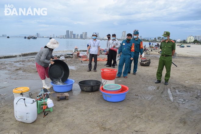 Lực lượng chức năng phường Thọ Quang (quận Sơn Trà) yêu cầu các tiểu thương sớm hoàn thành phân loại để rời khỏi khu vực bến cá tại bãi biển Bãi Ngang. Ảnh: HOÀNG HIỆP