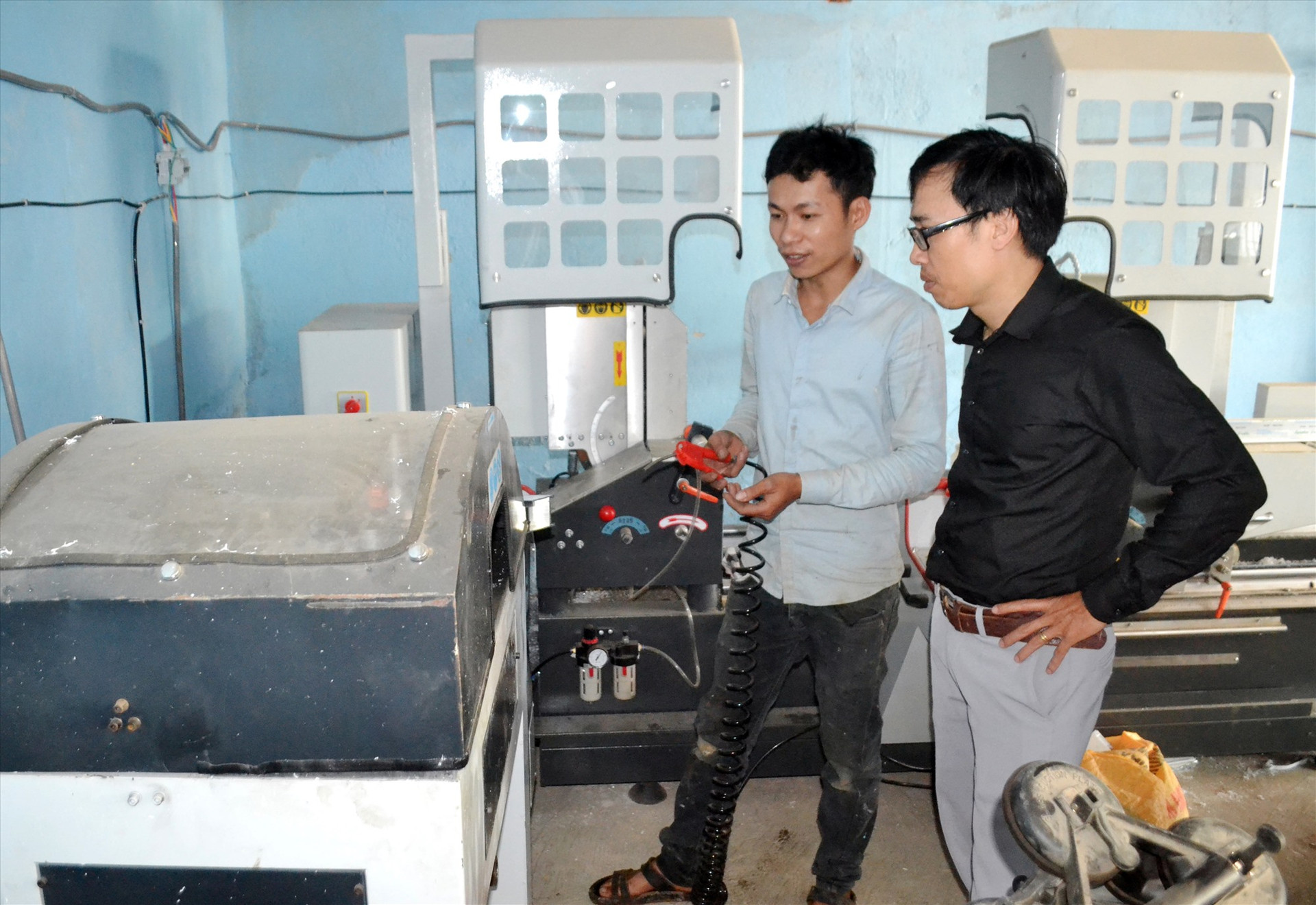 Anh Nguyễn Kim Đồng (áo sáng) ở thị trấn P’rao - điển hình lập nghiệp thành công - giới thiệu thiết bị ở cơ sở cửa nhôm của mình. Ảnh: KK