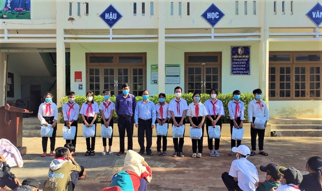 Ông A Ral Bói - Chủ tịch UBND xã Mà Cooih (bên phải) và thầy Ngô Văn Bừng - Hiệu trưởng Trường THCS xã Mà Cooih (bên trái) thay mặt Công ty Cổ phần Thuỷ điện A Vương trao tặng 146 bộ áo quần đồng phục quần xanh, áo trắng cho các em.