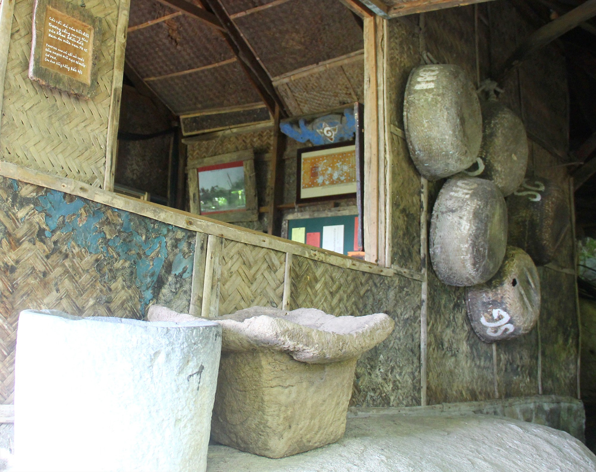 Chiếc cối đá lưu giữ tại Bảo tàng Đồng Đình, tấm bảng chép câu ca dao treo mé trên bên trái. Ảnh: H.X.H