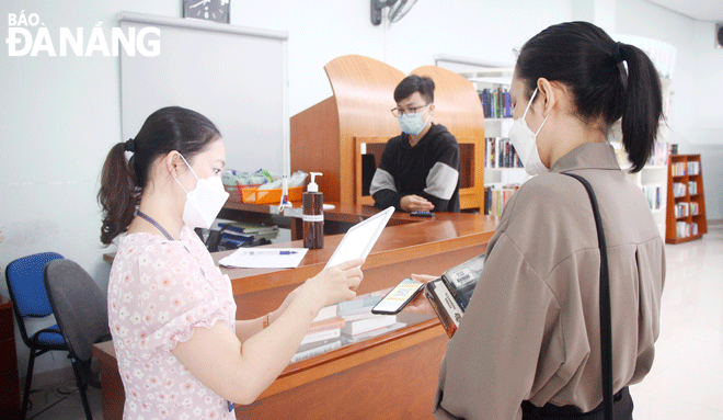 Cán bộ Thư viện Khoa học Tổng hợp Đà Nẵng (bên trái) quét mã QR khai báo y tế cho bạn đọc. Ảnh: XUÂN DŨNG